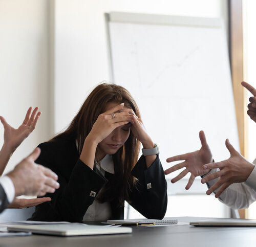 Frustrated millennial female worker sitting at table with colleagues, felling tired of working quarreling at business meeting. Upset stressed young businesswoman suffering from head ache at office.