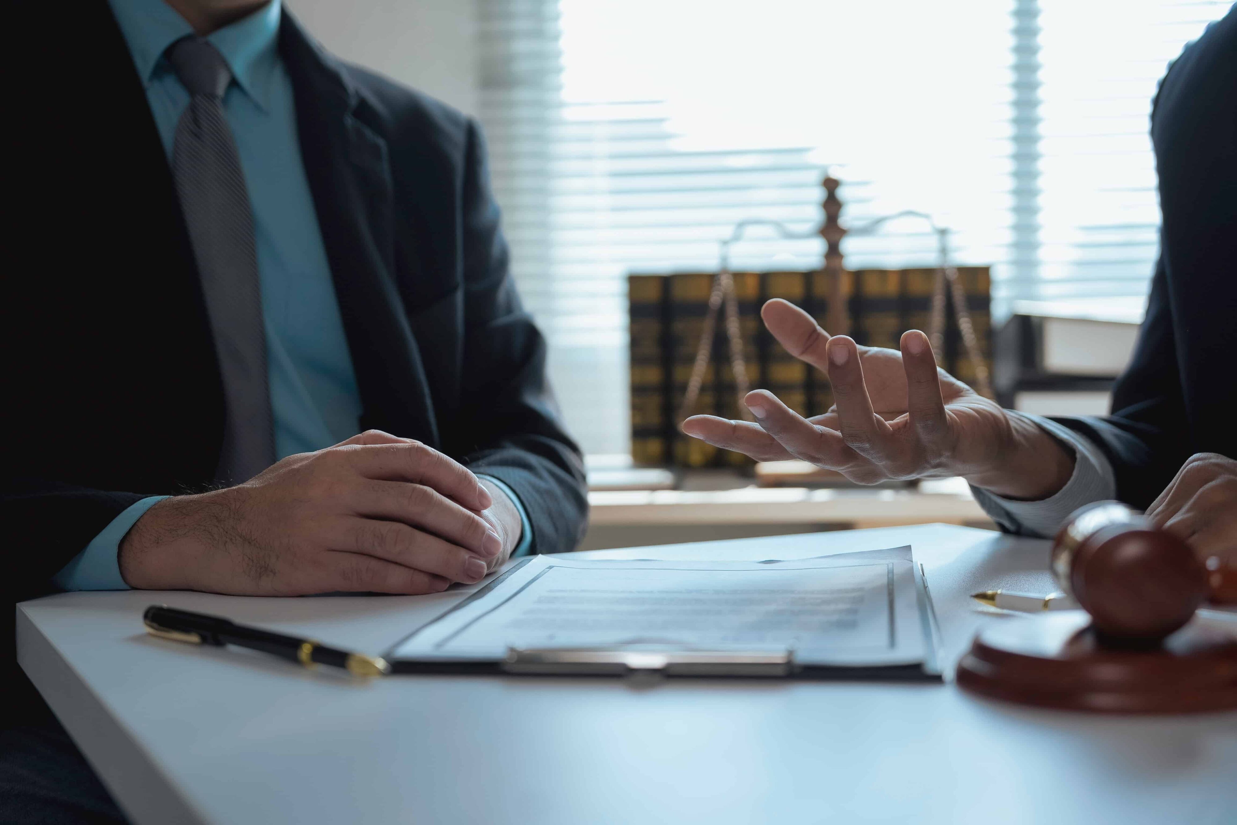 Lawyer consulting with client at desk with legal documents, gavel, and justice scales during a legal case discussion.
