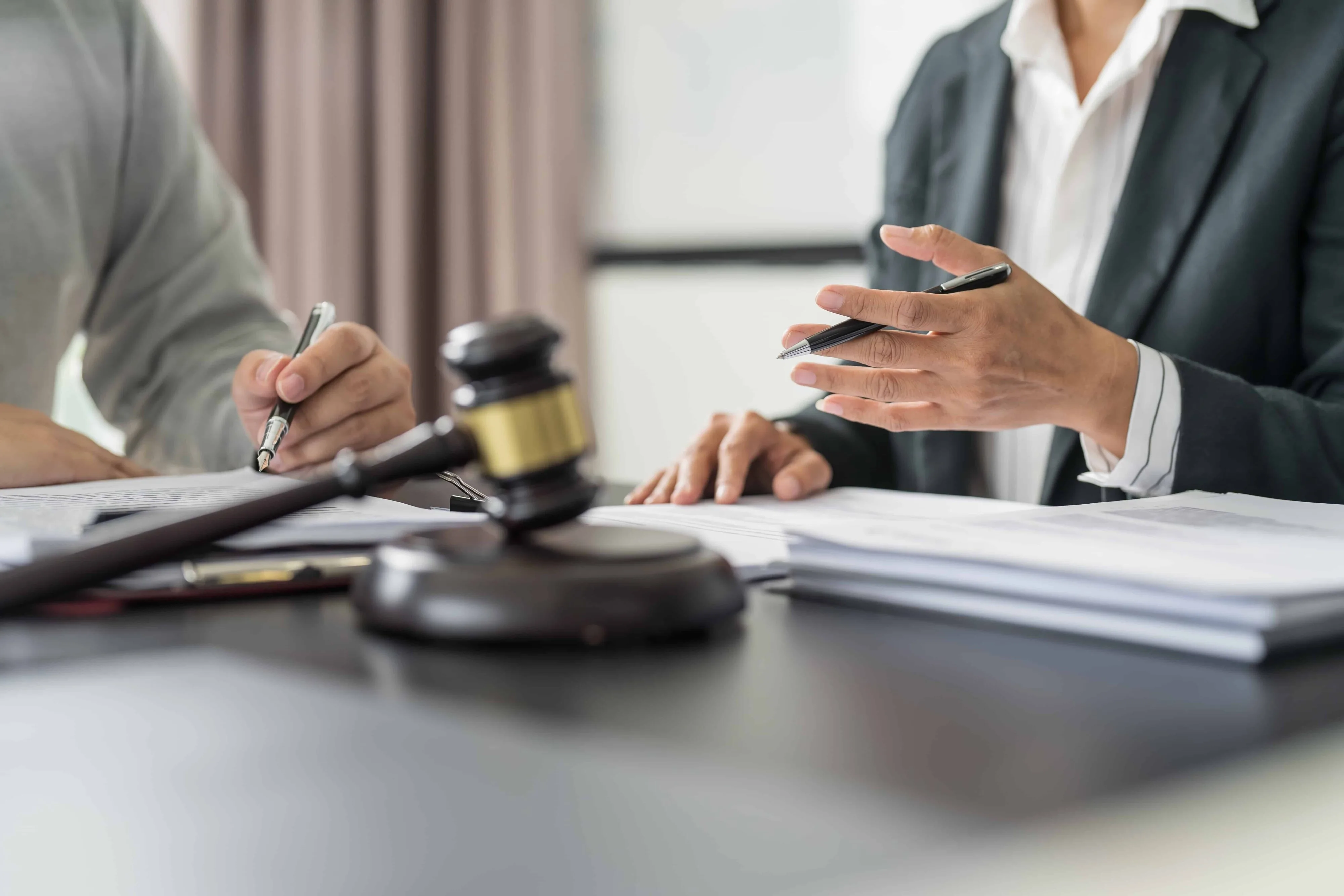 Lawyer consulting with client over legal documents at office desk with gavel in foreground.